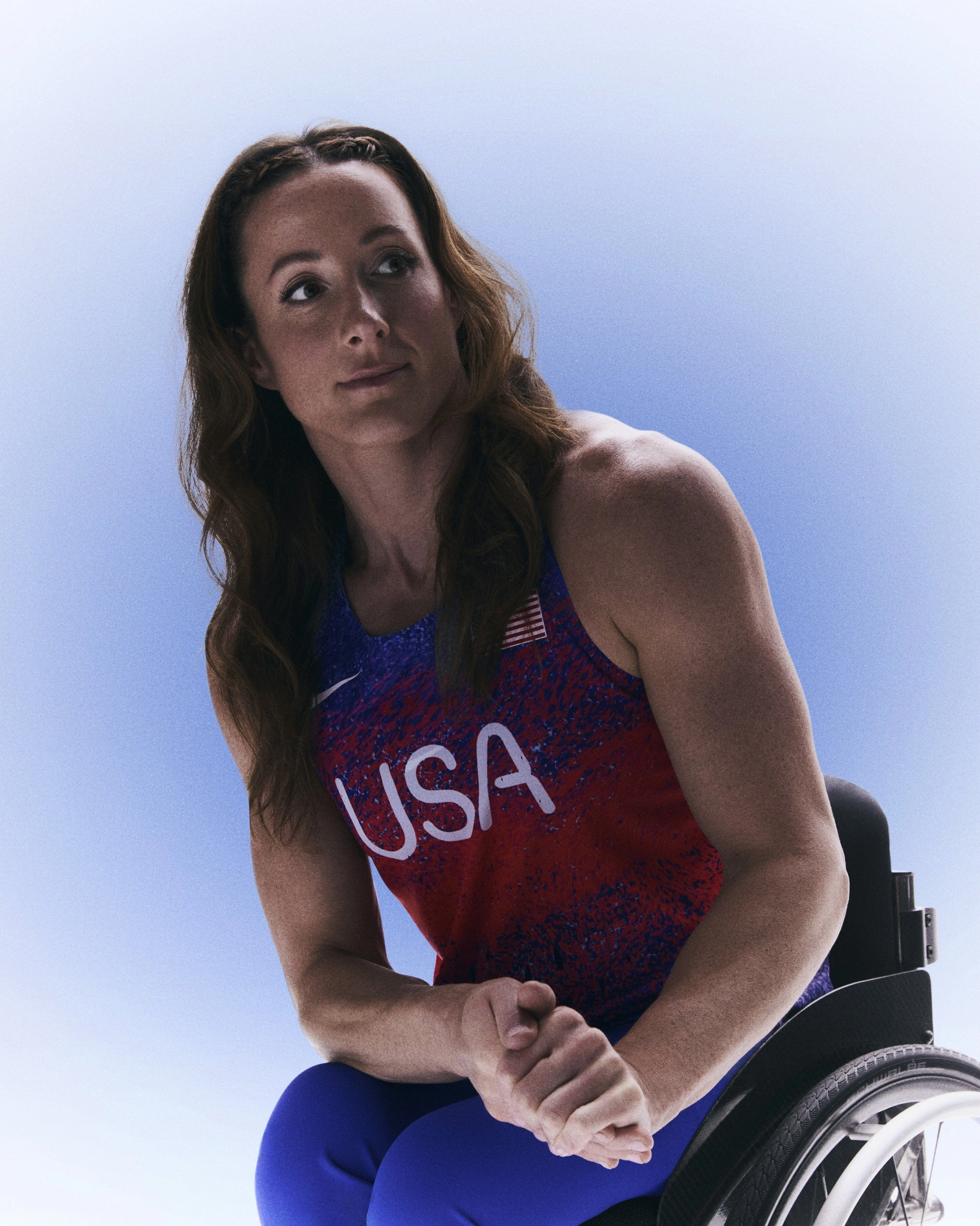 Tatyana McFadden leaning forward in her wheelchair with her hands clasped and wearing her USA track and field kit uniform.