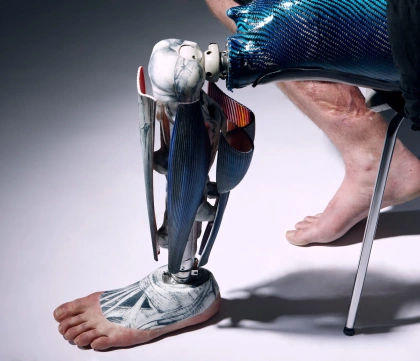 A person sits on a chair out of sight so that the image focuses on an anatomical prosthetic leg with blue muscles and a realistic looking partial foot