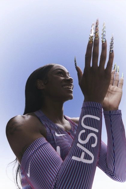 Upper body view of Sha'Carri Richardson clapping her hands and smiling while wearing her 2024 track and field kit uniform.